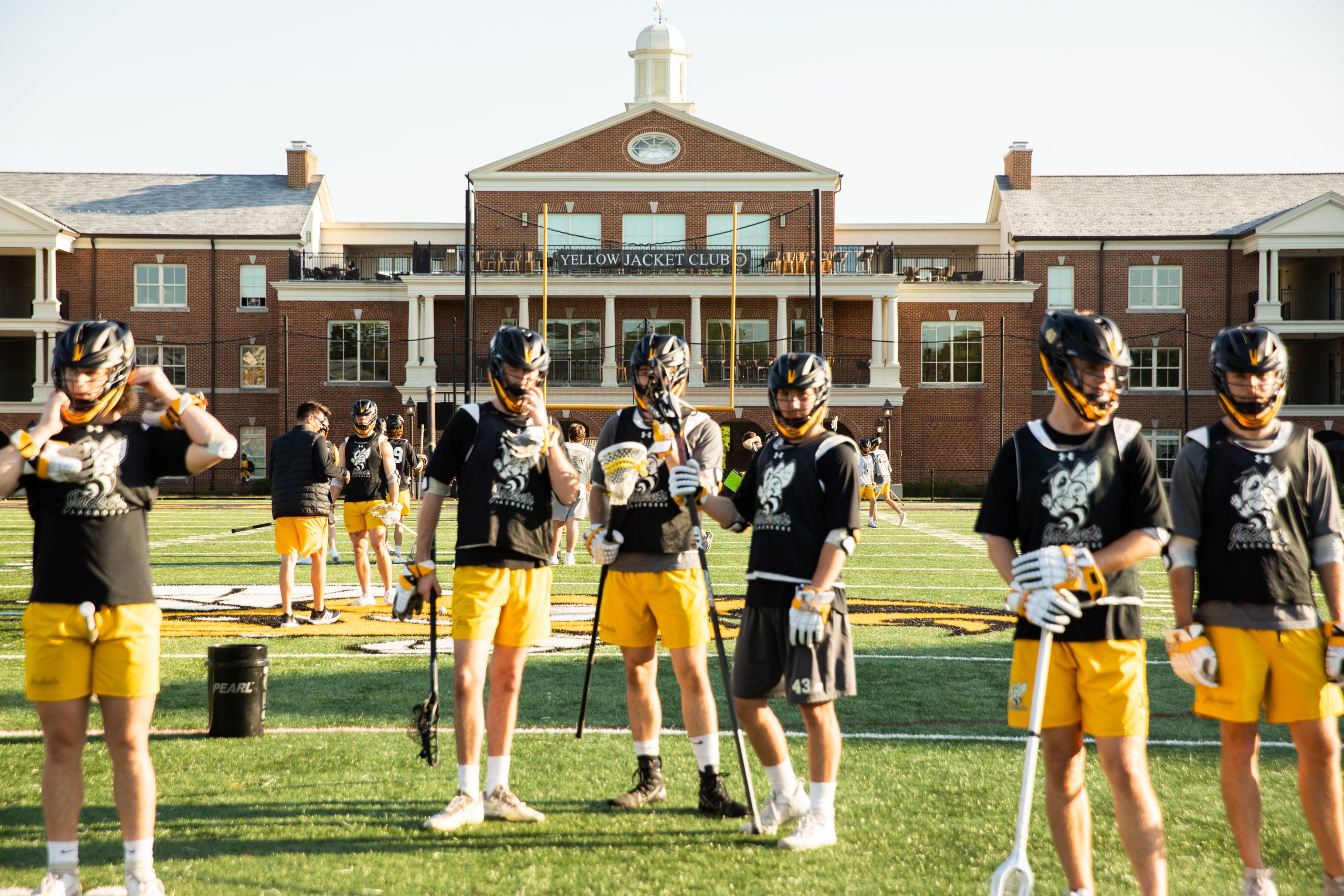 A group of RMC lacrosse players wearing black helmets and yellow shorts prepares for practice on Day Field.