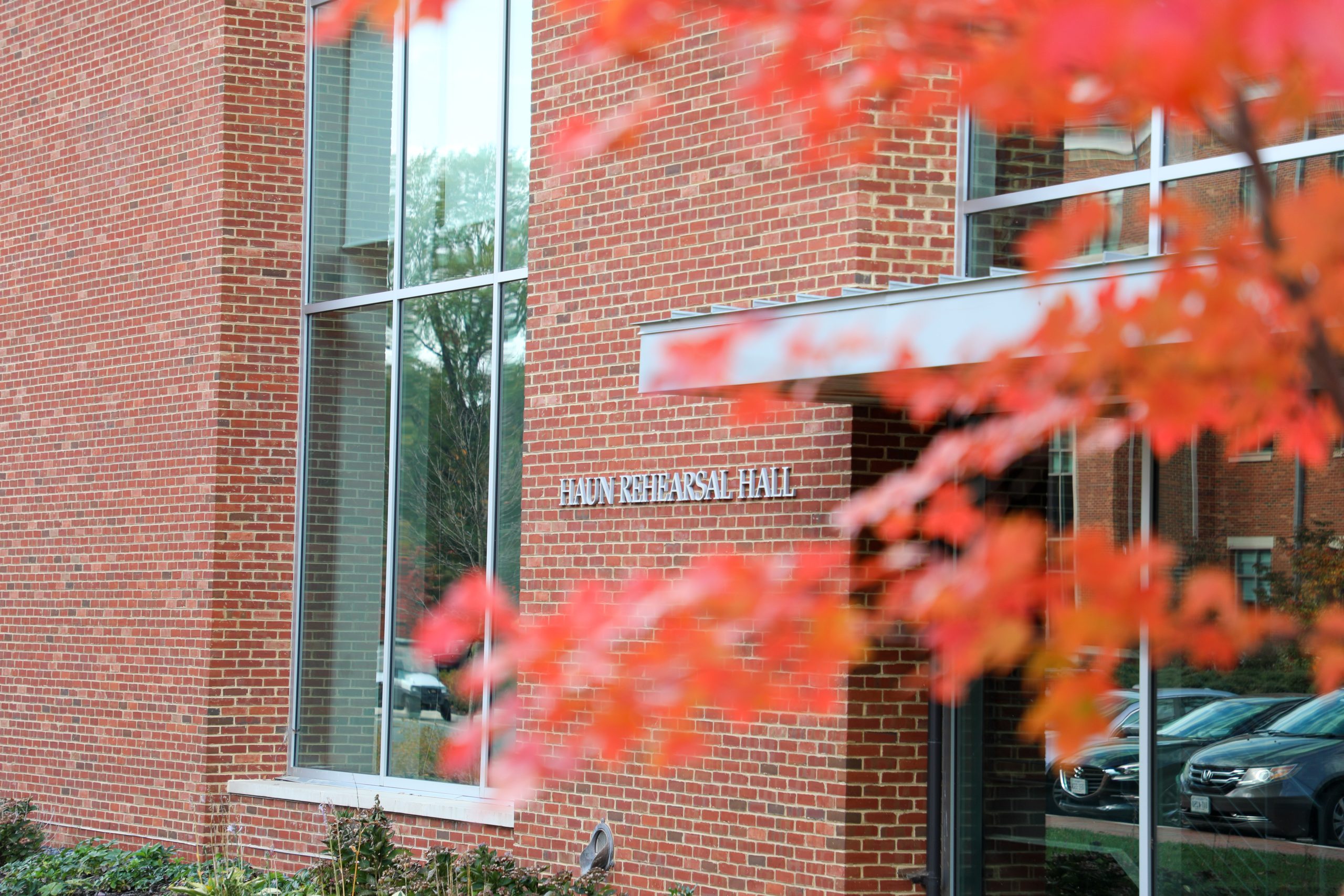 Brick building with a sign that reads "Haun Rehearsal Hall"; red autumn leaves are in the foreground.